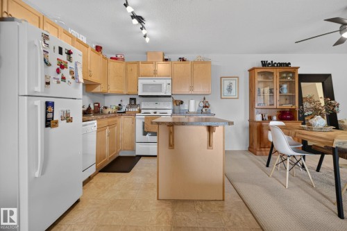 Kitchen featuring light wood cabinetry, white appliances, and a central island with a granite-look countertop - #335 2096 Blackmud Creek Dr Sw, Edmonton, AB - Indoor Photo Showing Kitchen