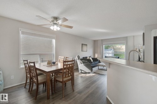 Open-concept living space featuring a wood-finish plank floor throughout, ceiling fan with integrated lighting, and abundant natural light from multiple windows with horizontal blinds - 15618 141 Street Nw, Edmonton, AB 