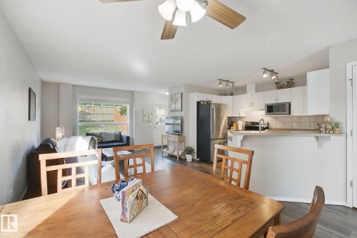 Open-concept living space featuring wood-finish flooring, a contemporary ceiling fan, and a kitchen with white cabinetry, stainless steel appliances, and a tiled backsplash - 15618 141 Street Nw, Edmonton, AB 