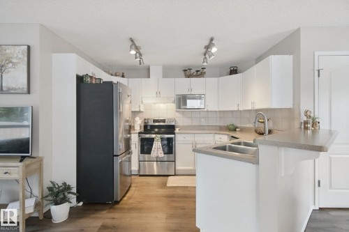 Kitchen featuring white cabinetry, stainless steel appliances, a double basin sink, light-toned countertops, and wood-finish flooring - 15618 141 Street Nw, Edmonton, AB 