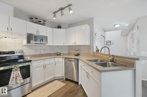 White cabinetry with brushed nickel hardware, stainless steel appliances, wood-finish flooring, and a double basin sink - 15618 141 Street Nw, Edmonton, AB 