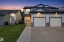 Two-story residence featuring light-colored siding, a two-car garage with brick detailing, a concrete driveway, and a front walkway leading to the entrance - 15618 141 Street Nw, Edmonton, AB 