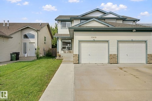 Two-story property featuring light-colored siding, a dark roof, and a two-car garage with white doors - 15618 141 Street Nw, Edmonton, AB 