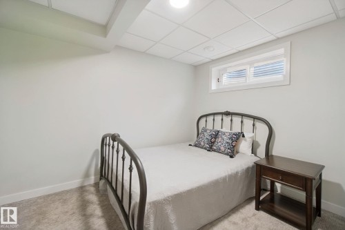 Finished basement bedroom featuring metal bed frame, wood-finish nightstand, recessed ceiling lighting, and high horizontal window for natural light - 15618 141 Street Nw, Edmonton, AB 