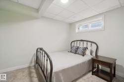 Finished basement bedroom featuring metal bed frame, wood-finish nightstand, recessed ceiling lighting, and high horizontal window for natural light - 