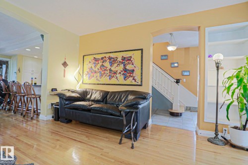 Hardwood flooring, arched doorway, staircase with white railing, built-in shelving, and a kitchen counter with bar seating - 10814 125 Street Nw, Edmonton, AB 