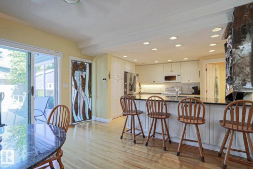 Wood-finish flooring throughout, white cabinetry with under-cabinet lighting, black countertops, and recessed lighting - 10814 125 Street Nw, Edmonton, AB 
