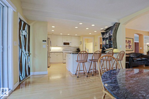 Recessed lighting illuminating the kitchen with white cabinetry, stainless steel appliances, and a central island with countertop seating - 10814 125 Street Nw, Edmonton, AB 