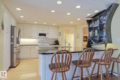 Kitchen featuring white cabinetry, stainless steel appliances, recessed lighting, a stone-finish countertop island, and wood-finish flooring - 10814 125 Street Nw, Edmonton, AB 