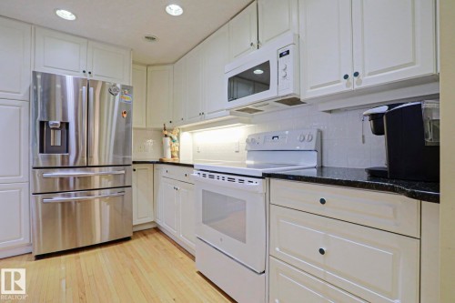 White cabinetry, stainless steel refrigerator, dark countertops, white tile backsplash, and wood-finish flooring - 10814 125 Street Nw, Edmonton, AB 