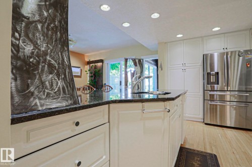Gourmet kitchen featuring a center island with sink, dark stone countertop, white cabinetry, stainless steel refrigerator, and recessed lighting - 10814 125 Street Nw, Edmonton, AB 