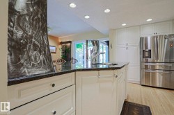 Gourmet kitchen featuring a center island with sink, dark stone countertop, white cabinetry, stainless steel refrigerator, and recessed lighting - 