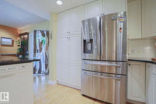 Stainless steel French door refrigerator, white panel cabinetry, black stone countertops, wood-finish flooring, white dishwasher - 10814 125 Street Nw, Edmonton, AB 
