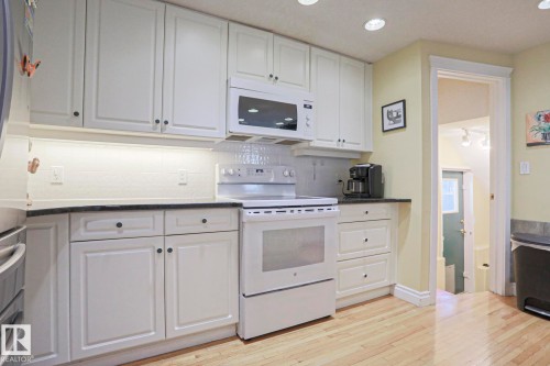 White cabinetry with recessed panel doors, dark countertops, white subway tile backsplash, and light wood-finish flooring - 10814 125 Street Nw, Edmonton, AB 