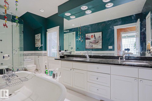 Dual basin vanity with stone countertop, white shaker cabinetry, freestanding bathtub, glass-enclosed shower, and recessed lighting - 10814 125 Street Nw, Edmonton, AB 