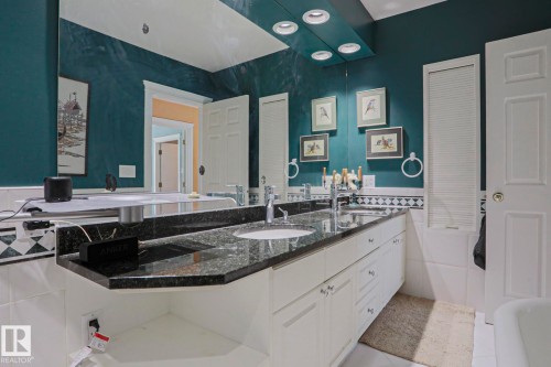 Dual basin vanity with a dark speckled countertop, white cabinetry, and a full-width mirror with integrated lighting - 10814 125 Street Nw, Edmonton, AB 
