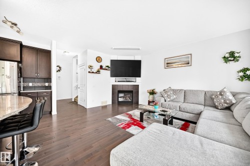 Hardwood-finish flooring, built-in fireplace, dark wood cabinetry, integrated kitchen island, and light wall finishes - 2015 Chalmers Way Sw, Edmonton, AB 