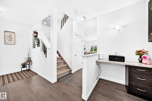 Wood-finish flooring, staircase with carpeted treads and white risers, built-in desk with stone countertop, dark wood-finish cabinetry, and contemporary wall sconce - 2015 Chalmers Way Sw, Edmonton, AB 