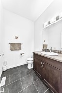 Dark-toned floor tiling, white walls, and a vanity with a light-toned countertop and integrated sink - 