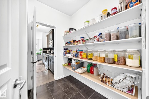 Walk-in pantry with extensive shelving, dark tile flooring, and a white paneled door - 2015 Chalmers Way Sw, Edmonton, AB 