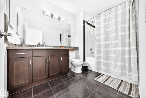 Bathroom featuring dark tile flooring, a dark wood-finish vanity with ample storage, a light-toned countertop, a tile backsplash, and a tub/shower combination - 2015 Chalmers Way Sw, Edmonton, AB 