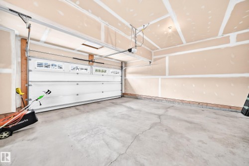 Spacious garage featuring a concrete floor, automatic garage door with upper window panels, and partial drywall finishes - 2015 Chalmers Way Sw, Edmonton, AB 