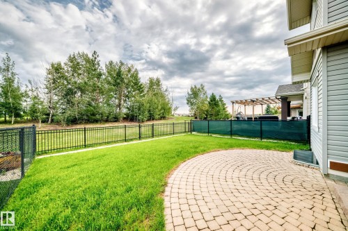 Expansive backyard featuring a manicured lawn, a curved paver patio, and a black wrought-iron fence - 2015 Chalmers Way Sw, Edmonton, AB 