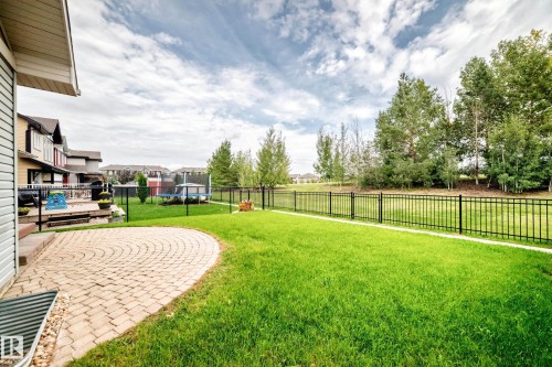 Expansive backyard featuring a circular paver patio, a wooden deck, a manicured lawn, and a black metal fence - 2015 Chalmers Way Sw, Edmonton, AB 