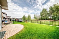 Expansive backyard featuring a circular paver patio, a wooden deck, a manicured lawn, and a black metal fence - 