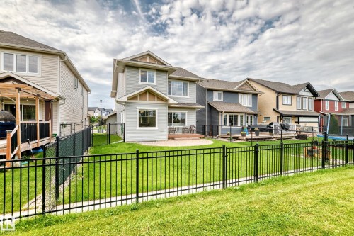 Two-story home with light-colored siding, a rear patio, and an expansive lawn - 2015 Chalmers Way Sw, Edmonton, AB 