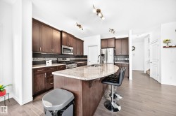 Spacious kitchen featuring dark wood cabinetry, stainless steel appliances, a large center island with a granite countertop, and light wood-finish flooring - 