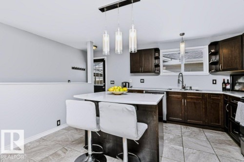 Kitchen featuring an island with a white countertop, dark wood-finish cabinetry, a window above the sink, and tile flooring - 18431 95A Avenue Nw, Edmonton, AB 