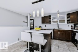 Kitchen featuring an island with a white countertop, dark wood-finish cabinetry, a window above the sink, and tile flooring - 