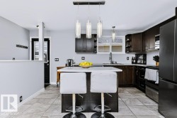 Kitchen featuring dark wood-finish cabinetry, light-toned tile flooring, a central island with a solid surface countertop, and pendant lighting fixtures - 