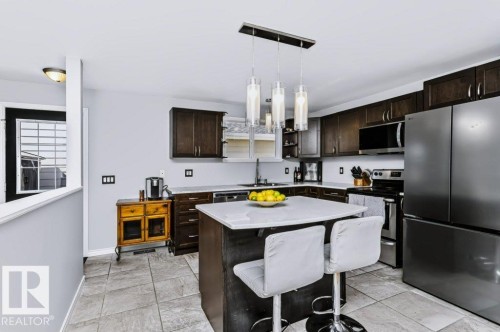 Kitchen featuring a central island with countertop, dark wood-finish cabinetry, stainless steel appliances, and tiled flooring - 18431 95A Avenue Nw, Edmonton, AB 
