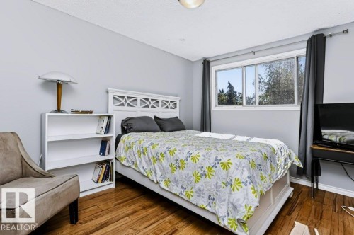 Wood-finish flooring with light gray wall paint, a white decorative headboard, a built-in white shelving unit, and a window with natural light - 18431 95A Avenue Nw, Edmonton, AB 