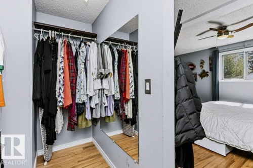 Recessed closet with a built-in hanging rod, full-length mirror, wood-finish flooring, and white trim - 18431 95A Avenue Nw, Edmonton, AB 