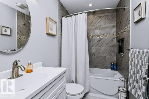 Bathroom featuring a full-size bathtub, tiled shower surround with mosaic accent, built-in shower niche, vanity with integrated sink, and an oval mirror - 18431 95A Avenue Nw, Edmonton, AB 