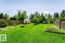 Expansive fenced yard featuring a storage shed, mature trees, and a dedicated garden plot - 18431 95A Avenue Nw, Edmonton, AB 