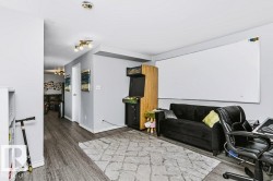 Spacious recreation room featuring wood-finish flooring, a large whiteboard wall, recessed lighting throughout, and built-in cabinetry - 
