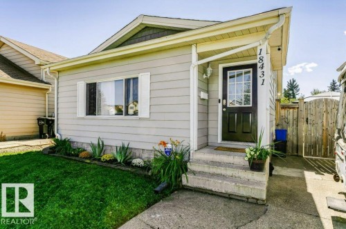 Light gray horizontal siding with white trim, a black front door with glass panels, and a concrete pathway - 18431 95A Avenue Nw, Edmonton, AB 