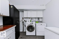 Dedicated laundry area featuring a front-load washer, dryer, wood-finish flooring, white upper cabinetry, and a built-in dark storage cabinet - 