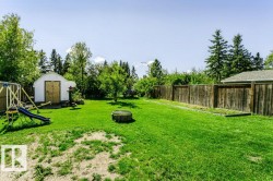 Expansive grassy yard featuring mature trees, a storage shed with double doors, and wood fencing - 