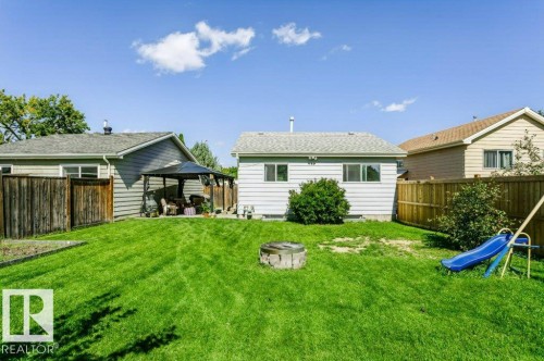 Expansive grassy yard featuring a fenced perimeter, a covered patio area, and a fire pit - 18431 95A Avenue Nw, Edmonton, AB 