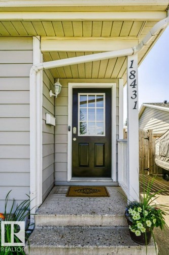 Covered front entryway with concrete steps, black paneled door with glass inserts, wall-mounted exterior light fixture, and vertical house numbers - 18431 95A Avenue Nw, Edmonton, AB 