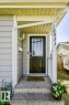 Covered front entryway with concrete steps, black paneled door with glass inserts, wall-mounted exterior light fixture, and vertical house numbers - 18431 95A Avenue Nw, Edmonton, AB 
