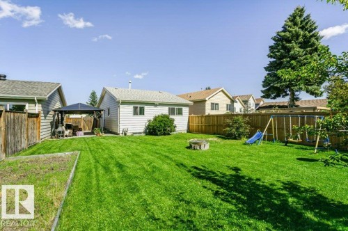 Expansive grassy yard with mature trees, established perimeter fencing, and a built-in fire pit - 18431 95A Avenue Nw, Edmonton, AB 