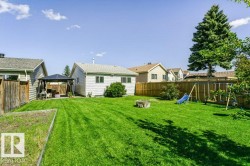 Expansive grassy yard with mature trees, established perimeter fencing, and a built-in fire pit - 