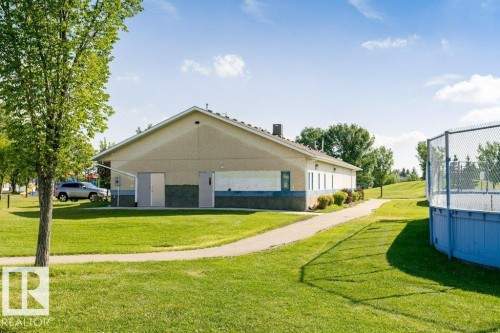Expansive green space featuring a paved pathway, mature trees, and a recreational court with fencing - 18431 95A Avenue Nw, Edmonton, AB 