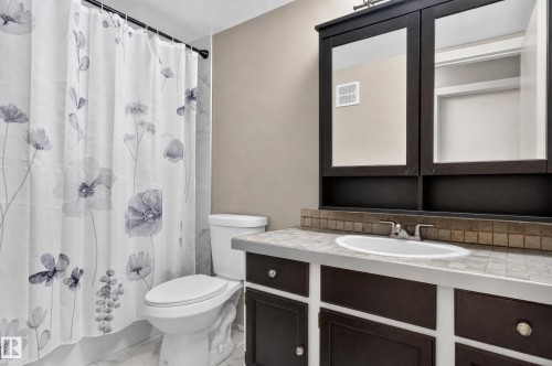 Dark wood-finish vanity with an integrated sink, mosaic tile backsplash, and mirrored medicine cabinet - #204 7407 171 St Nw, Edmonton, AB 